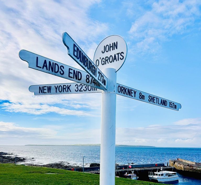 John O'Groats on the NC500 john O'Groats sign on NC500 with sea and harbour behind